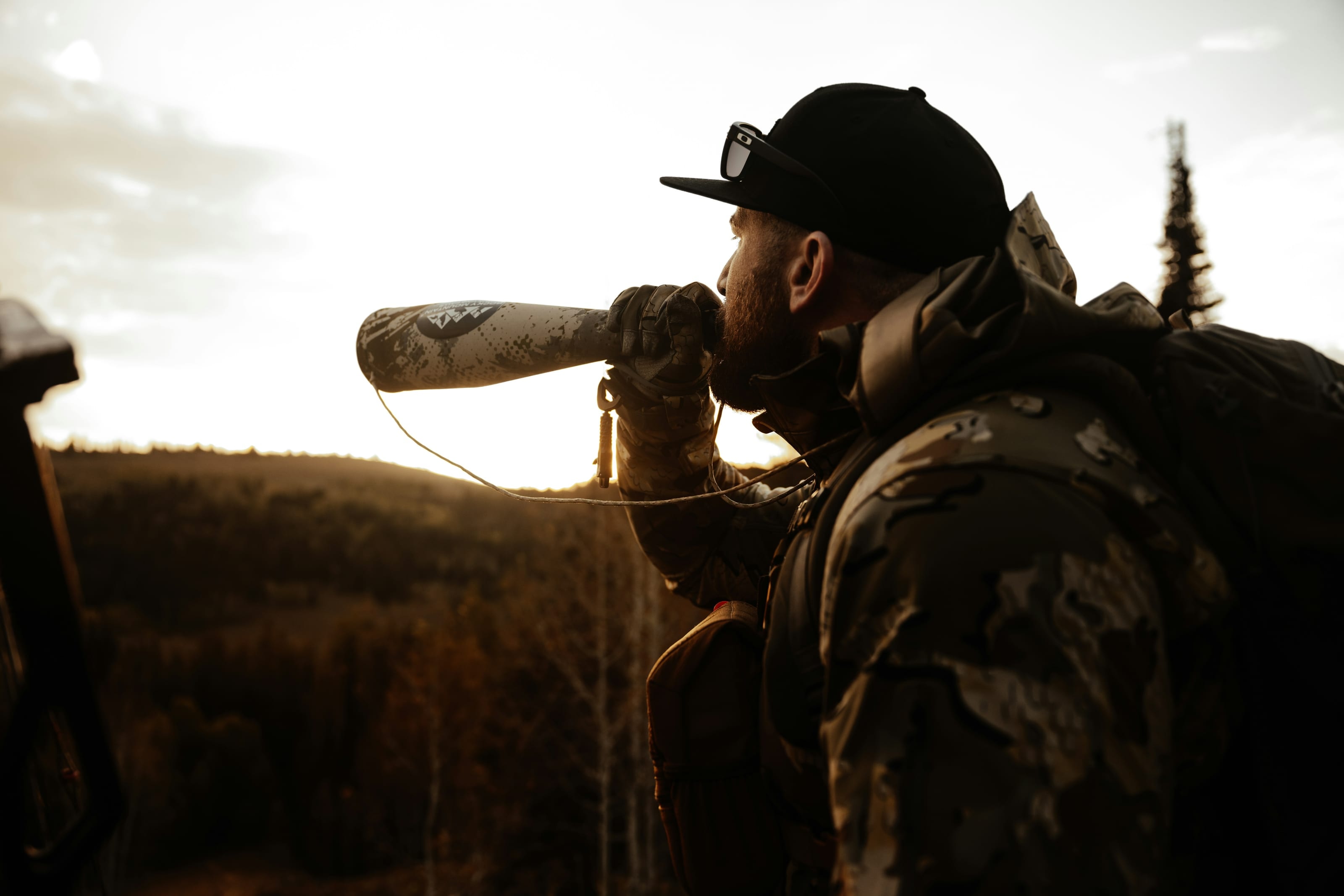 Hunter glassing a ridgeline through a spotting scope at sunrise